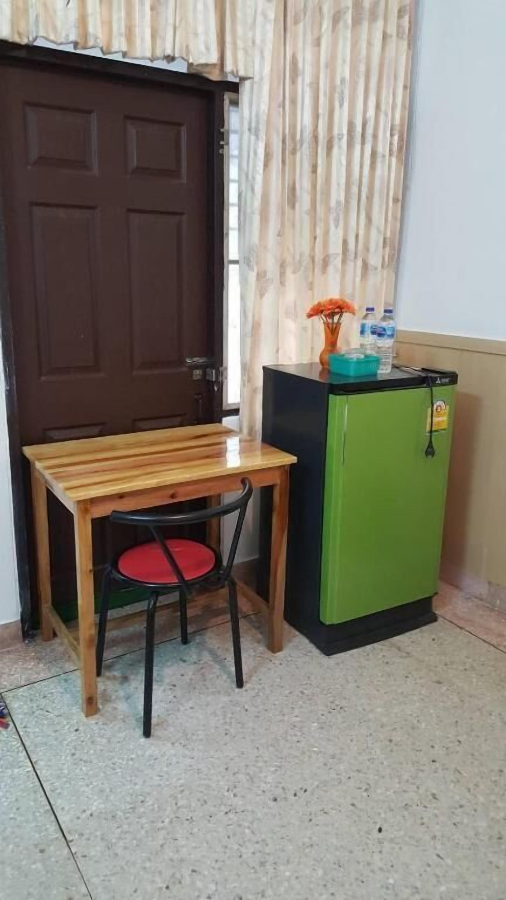 A small room with a wooden table and a single chair, a green refrigerator, and a brown door.