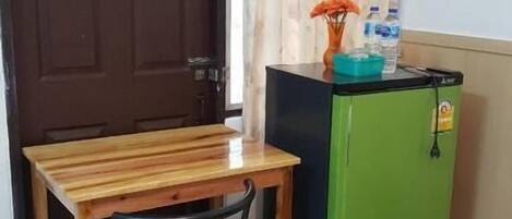 A small room with a wooden table and a single chair, a green refrigerator, and a brown door.