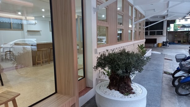 A modern interior with a large glass door, wooden panel walls, and a seating area with tables and chairs. - Sataya Apartment (Maha Sarakham)