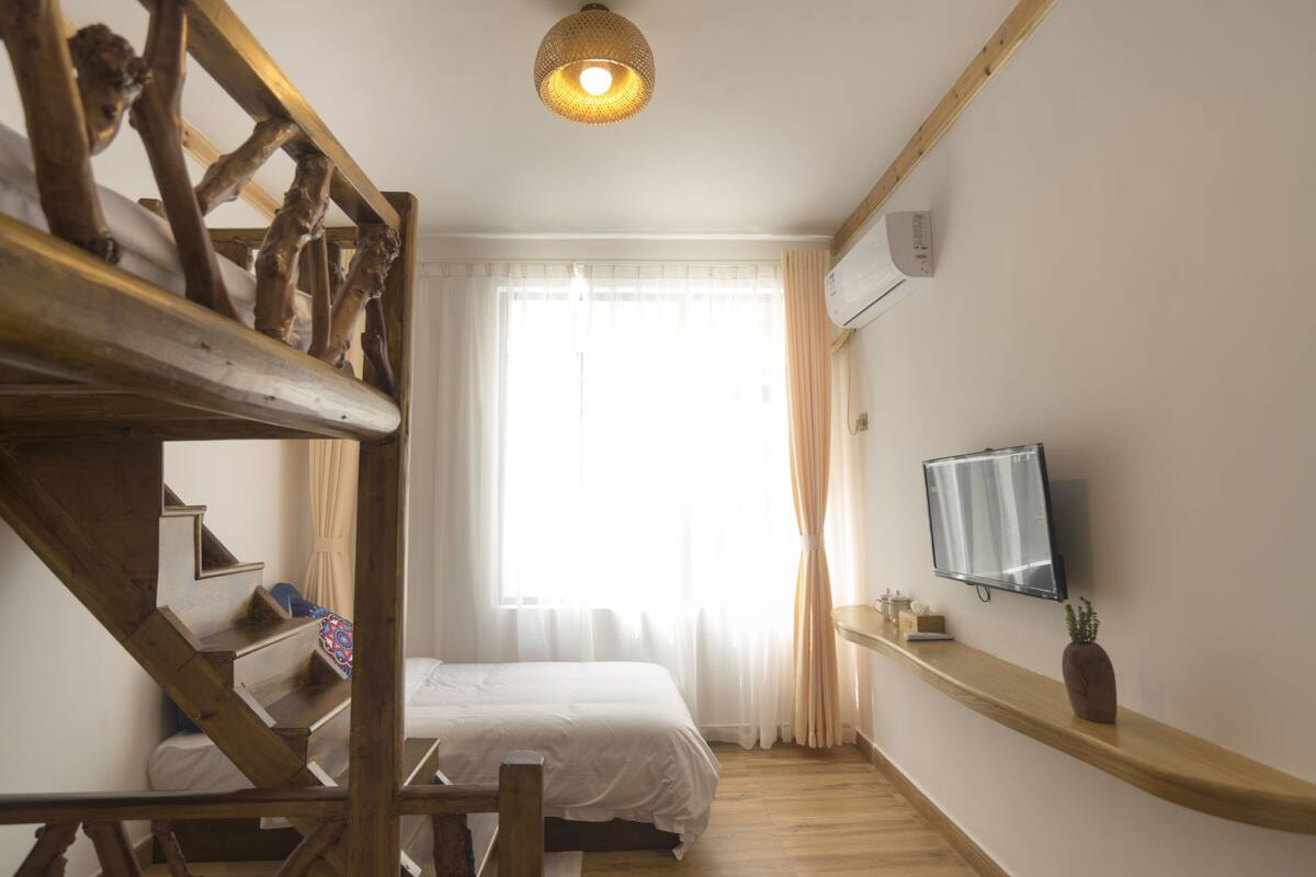Un dormitorio con cama, una escalera de madera, televisor y ventana con cortinas.