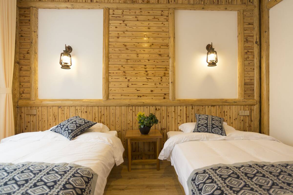 Habitación con dos camas, paneles de madera en las paredes y dos lámparas fijadas a la pared.