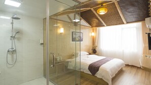 A modern bathroom with a glass shower enclosure, a toilet, and a bed with a wooden floor.