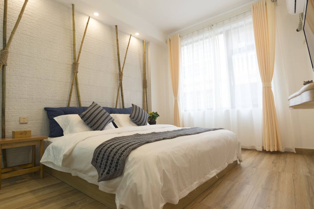Un dormitorio ordenado con una cama grande, cabecero de madera y una pared de ladrillo blanco.