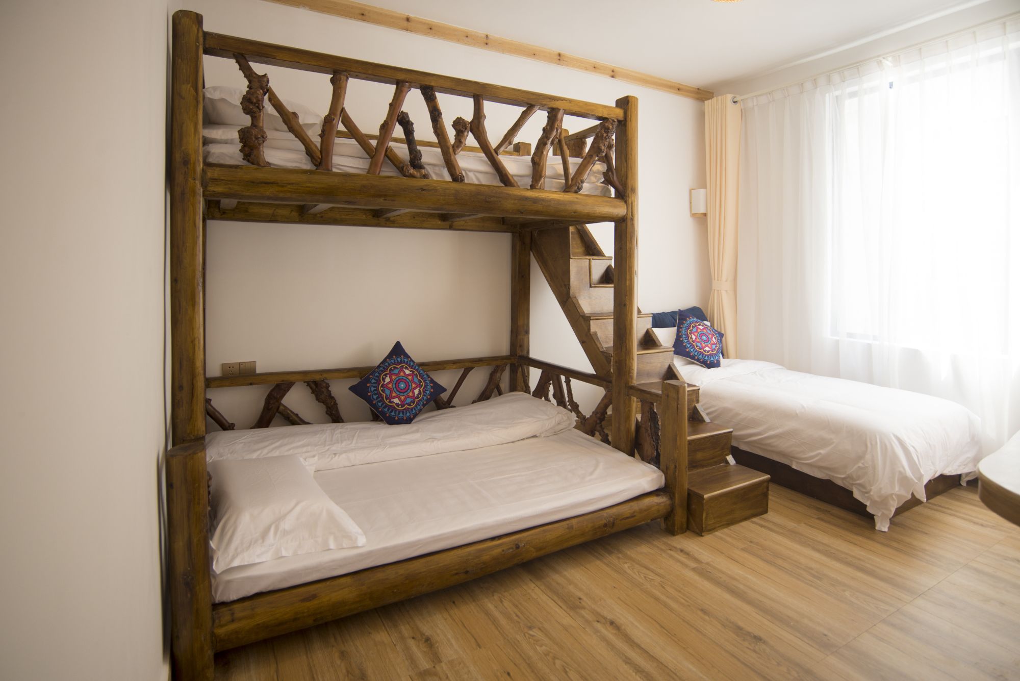 Ein Stockbett mit Holzbettgestell und weißer Bettwäsche, ein Fenster mit durchsichtigen Vorhängen und ein Holzboden.