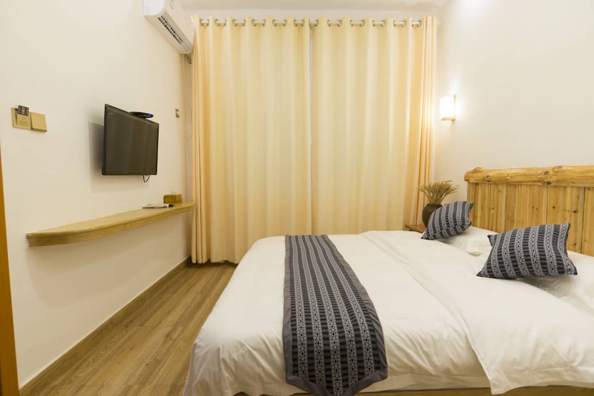 Habitación de hotel con cama, cabecera de madera, televisor montado, estante de madera y cortina.