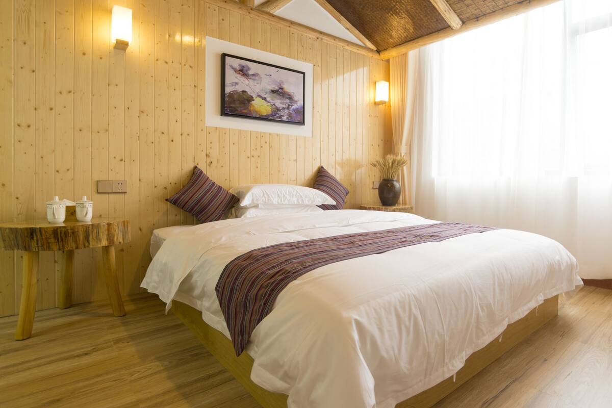 Un dormitorio con paneles de madera, una cama, almohadas, una mesita de noche y un cuadro en la pared.
