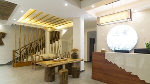 A reception area with a wooden reception desk, a round wall clock, and a staircase with bamboo railings.