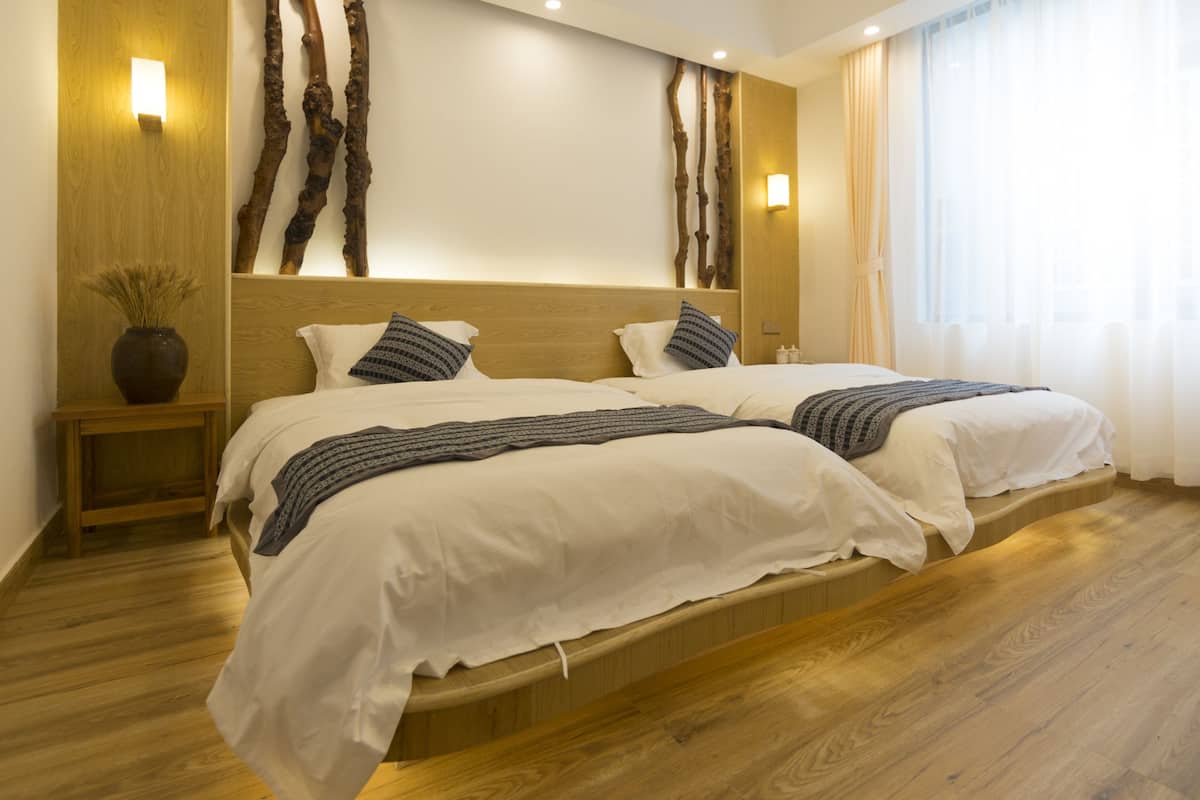 Una cama doble con cabecera de madera, dos mesitas de noche con lámparas y un ventanal con cortinas.
