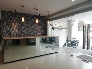 Un área de recepción con una pared de diseño, un mostrador de recepción y una puerta de vidrio que da al exterior.