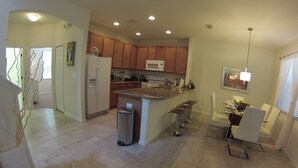 A modern kitchen with wooden cabinets, a central island, and a dining area with a white chair. - Aco63675 - Bella Vida Resort - 4 Bed 3 Baths Townhouse (Kissimmee)