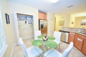 Eine kompakte Küche mit weißen Schränken, einem Edelstahlkühlschrank und einer Essecke mit einem Glastisch und weißen Stühlen.