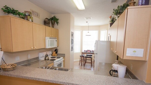 Una cocina con armarios de madera, microondas, estufa y comedor con sillas y mesa.