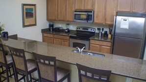 A kitchen with wooden cabinets, a granite countertop, a stainless steel refrigerator, a microwave, a stove, and a sink. - Ip60387 - Paradise Palms - 5 Bed 4 Baths Townhome (Kissimmee)