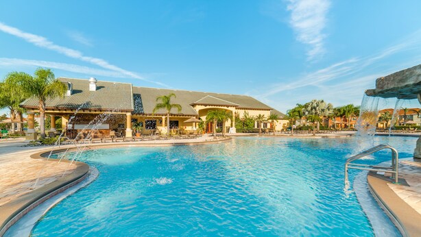 A swimming pool with a waterfall feature, surrounded by palm trees and a building with a tiled roof. - Ip60387 - Paradise Palms - 5 Bed 4 Baths Townhome (Kissimmee)