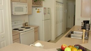 Une cuisine équipée d’un four à micro-ondes, d’une cuisinière, d’un réfrigérateur et d’un panier à fruits posé sur le plan de travail.