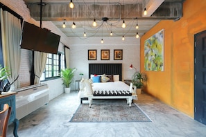 A bedroom with a bed, a desk, a chair, a TV, and a large painting on the wall.