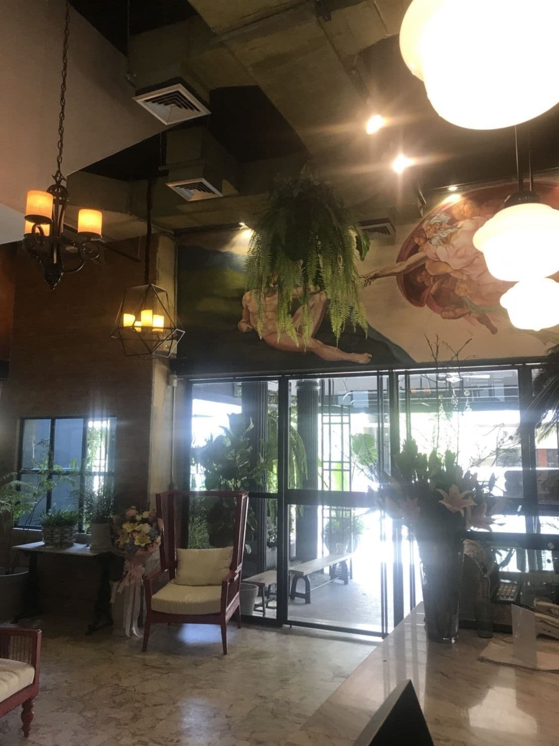 A spacious room with a large window, a hanging plant, a chandelier, and a wooden chair.