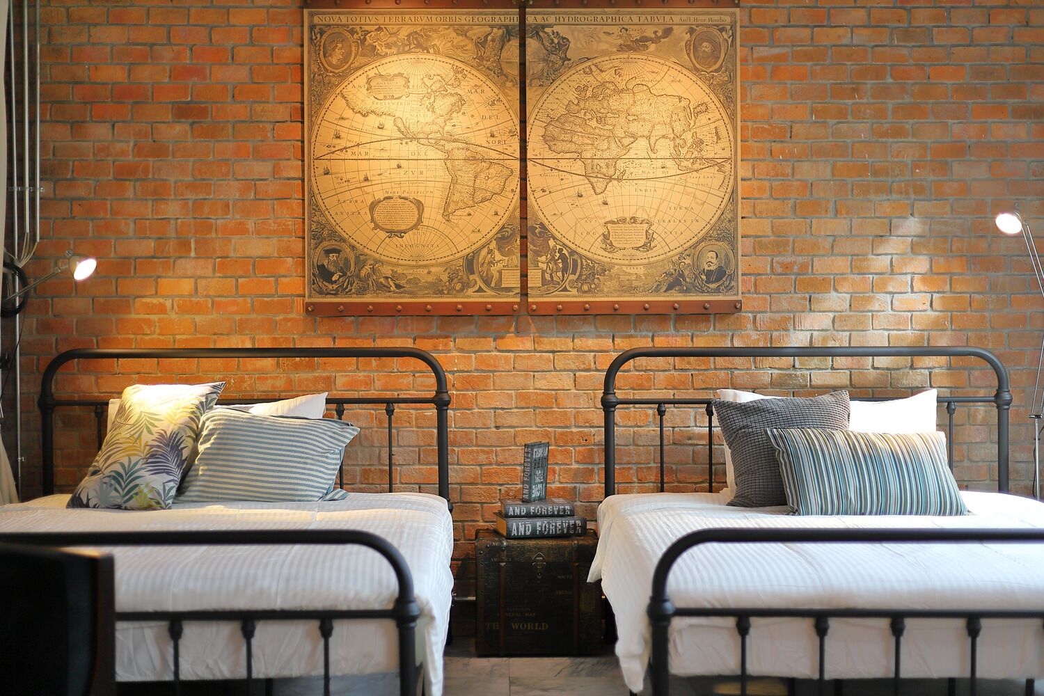 A room with two beds, a brick wall, and a large map.