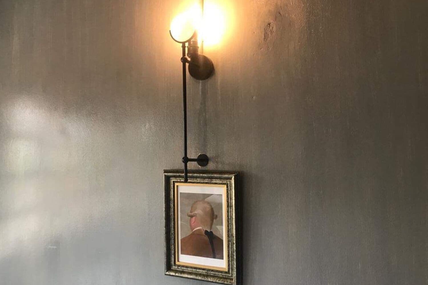 A wall-mounted light fixture with a single bulb and a framed picture below it.