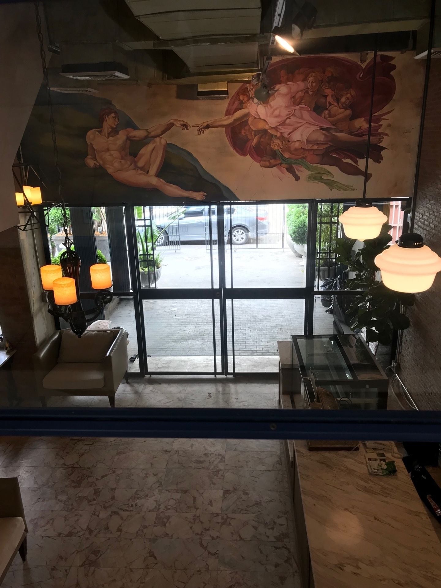 A restaurant interior with marble flooring, hanging pendant lights, a mural of cherubs, and a view of the street through glass doors.