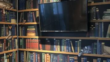 A library with bookshelves, a flat-screen TV mounted on the wall, and a wooden table with a remote control.
