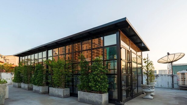 Un bâtiment moderne doté de grandes fenêtres en verre, de jardinières en béton ornées de plantes et d’une antenne parabolique.