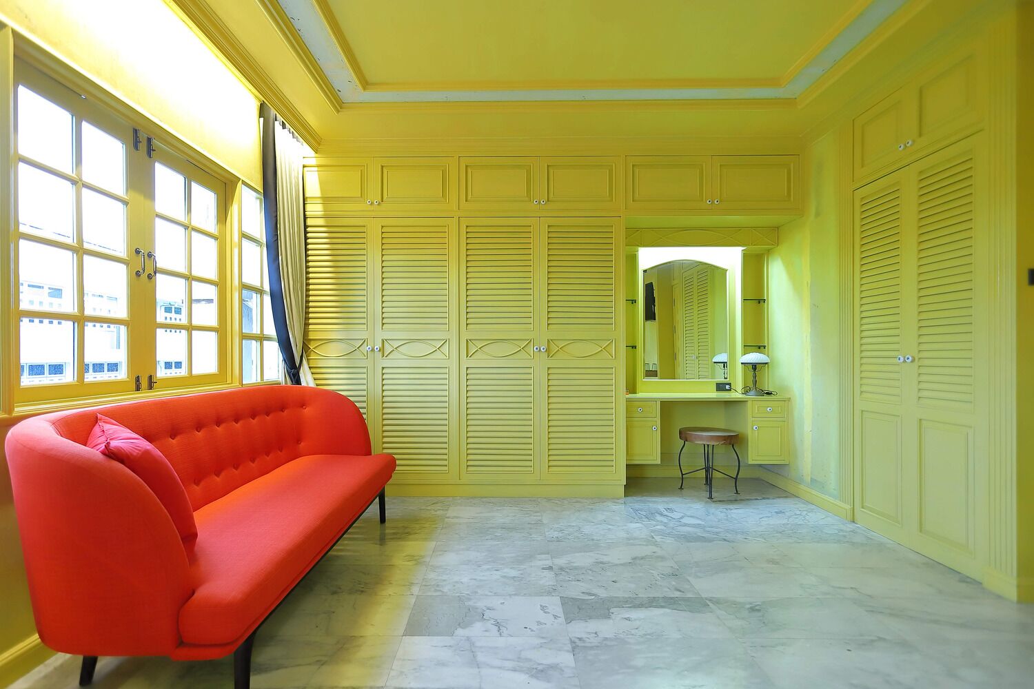A room with a yellow wall, a red sofa, a vanity with a mirror, and a small stool.