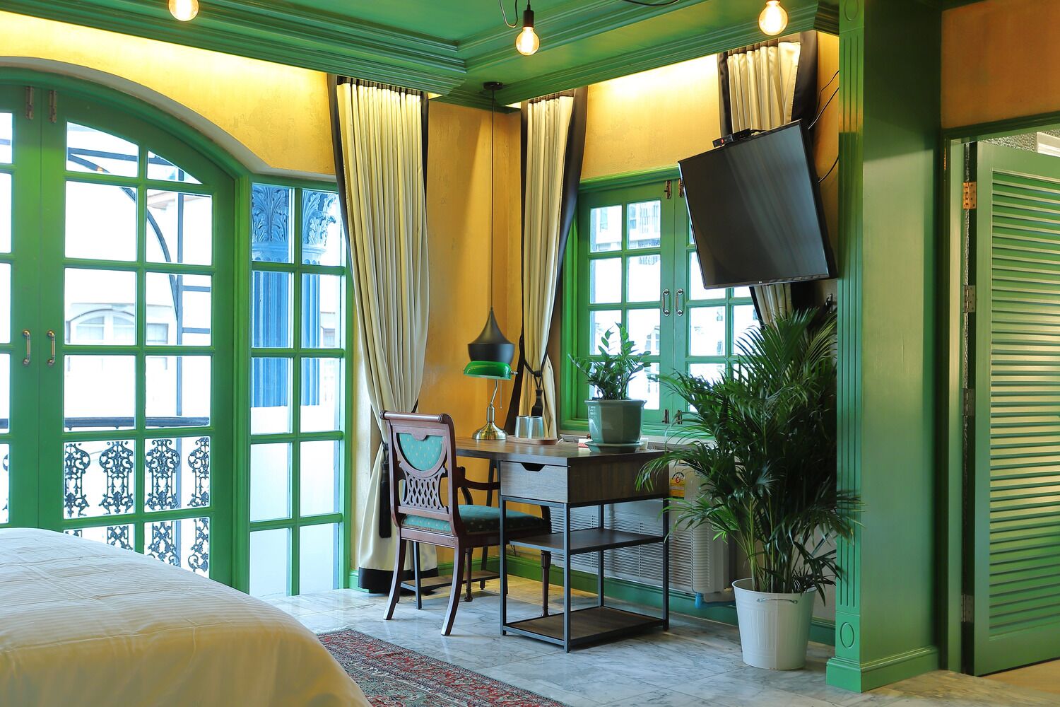 A room with a bed, a desk with a chair, a television, and large windows with curtains.