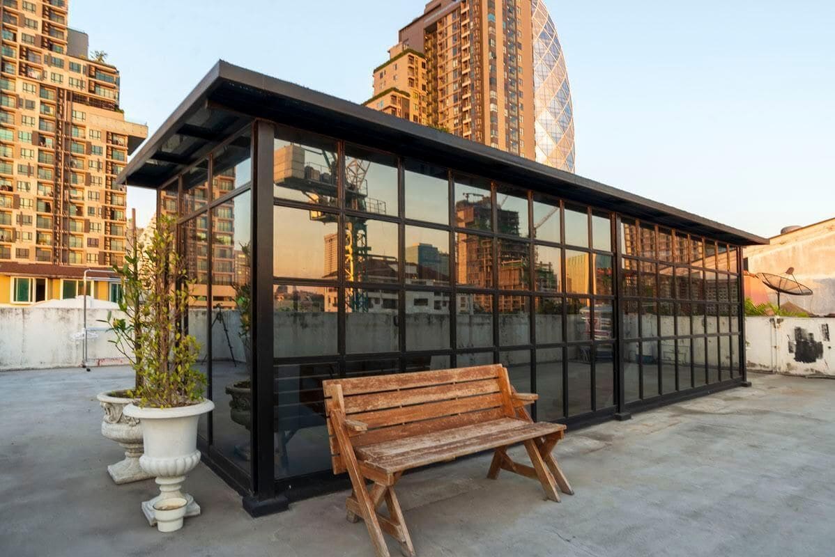 A modern glass building with a bench and potted plants.