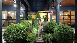 Un intérieur moderne avec un jardin central agrémenté d’une statue, entouré de plantes en pot et d’un mur de briques.