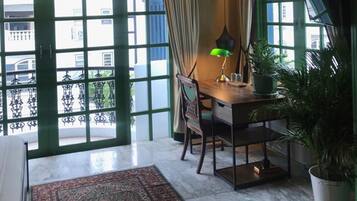 A room with a large window, a desk with a lamp, a chair, a rug, and a potted plant.