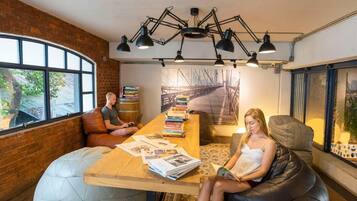A modern room with a brick wall, large windows, a wooden table with books, and a black leather couch.