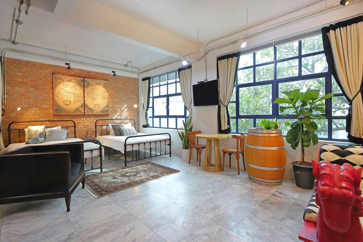 Une pièce comprenant un lit, une table à manger avec des chaises, un canapé rouge, une grande fenêtre avec des rideaux et une plante en pot.
