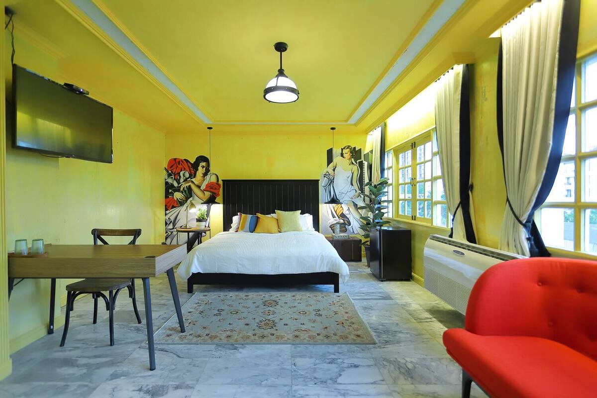 Une chambre d’hôtel équipée d’un lit, d’un bureau, d’une chaise, d’une télévision et d’une grande fenêtre avec des rideaux.