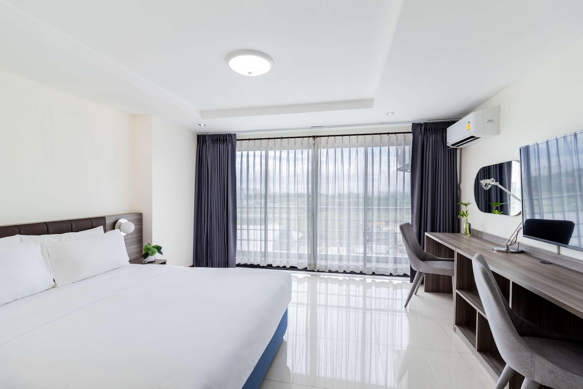 Une chambre d’hôtel avec un grand lit, un bureau avec une chaise, une lampe de bureau et une fenêtre avec des rideaux.