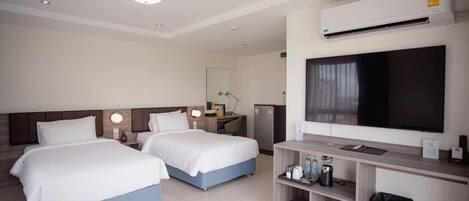 A hotel room with two beds, a desk with a flat-screen TV, a minibar, and a trash bin.