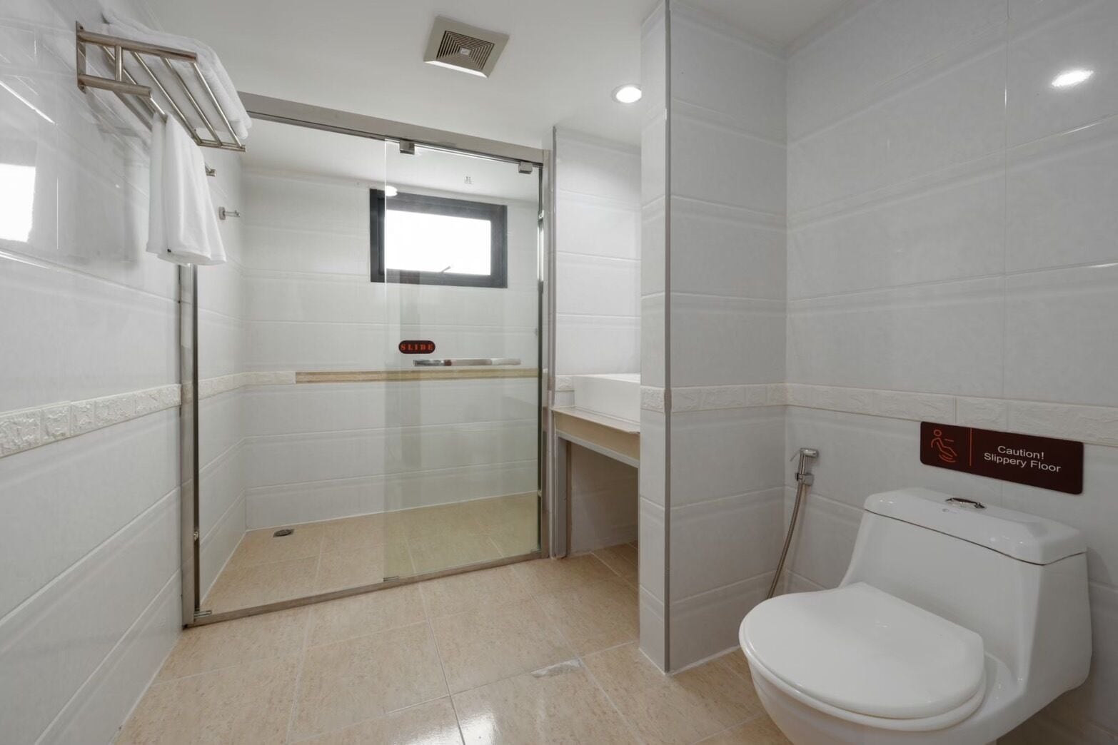 A modern bathroom with a glass shower enclosure, a toilet, and a caution sign for a slippery floor.