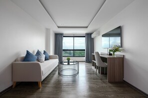 A modern living room with a sofa, coffee table, and a dining area with a desk and chair. - SureStay By Best Western Iconic Suvarnabhumi (Bang Sao Thong)