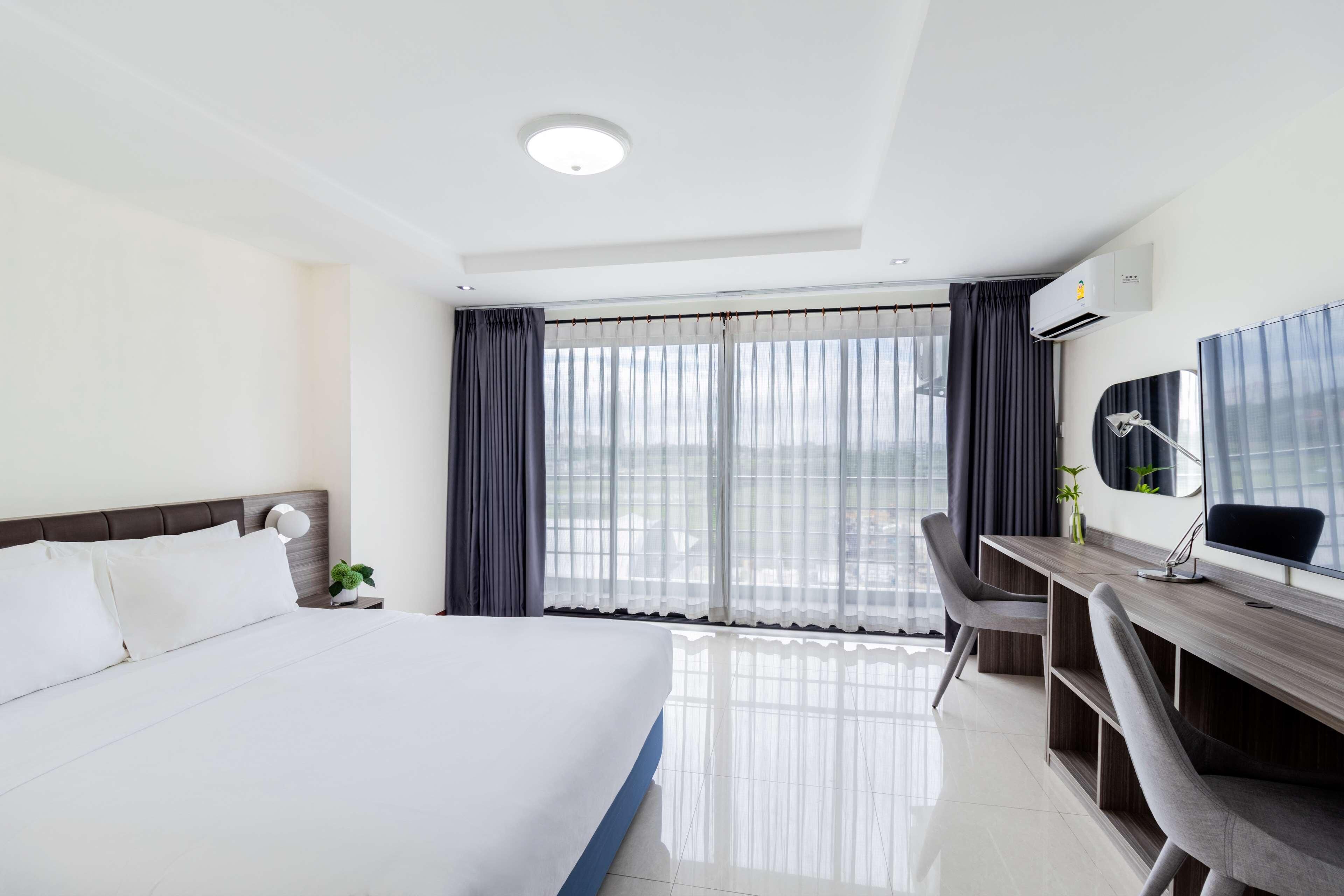 Een hotelkamer met een groot bed, een bureau met stoel, een bureaulamp en een raam met gordijnen.