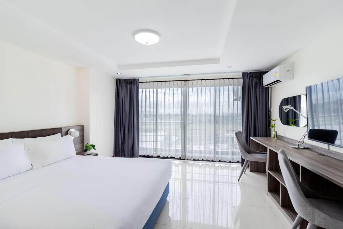 A hotel room with a large bed, a desk with a chair, a desk lamp, and a window with curtains.