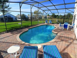 Une piscine couverte, avec des chaises bleues et une table, entourée d’une terrasse en briques.