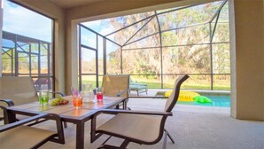 A covered patio with a table and chairs, a pool, and a view of trees. - Aco244924 - Paradise Palms Resort - 6 Bed 5 Baths Villa (Kissimmee)