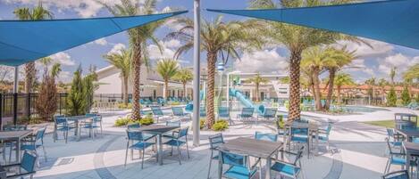 An outdoor patio area with blue umbrellas, seating, and palm trees.