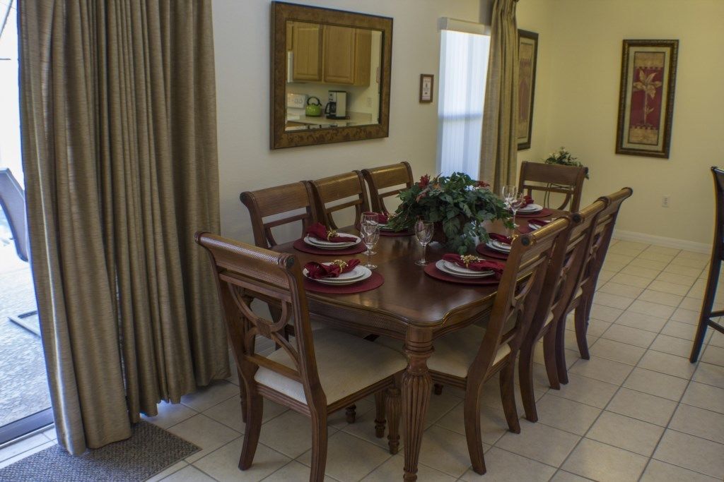 A dining room with a wooden table set for six, surrounded by six wooden chairs. A large mirror hangs on the wall above the table.