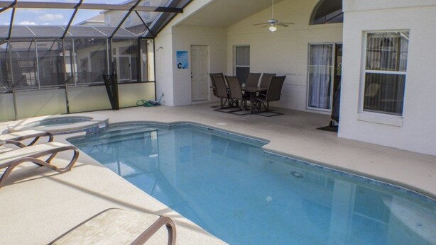 Una piscina interior con sillas de descanso, un ventilador de techo y un comedor con mesa y sillas.