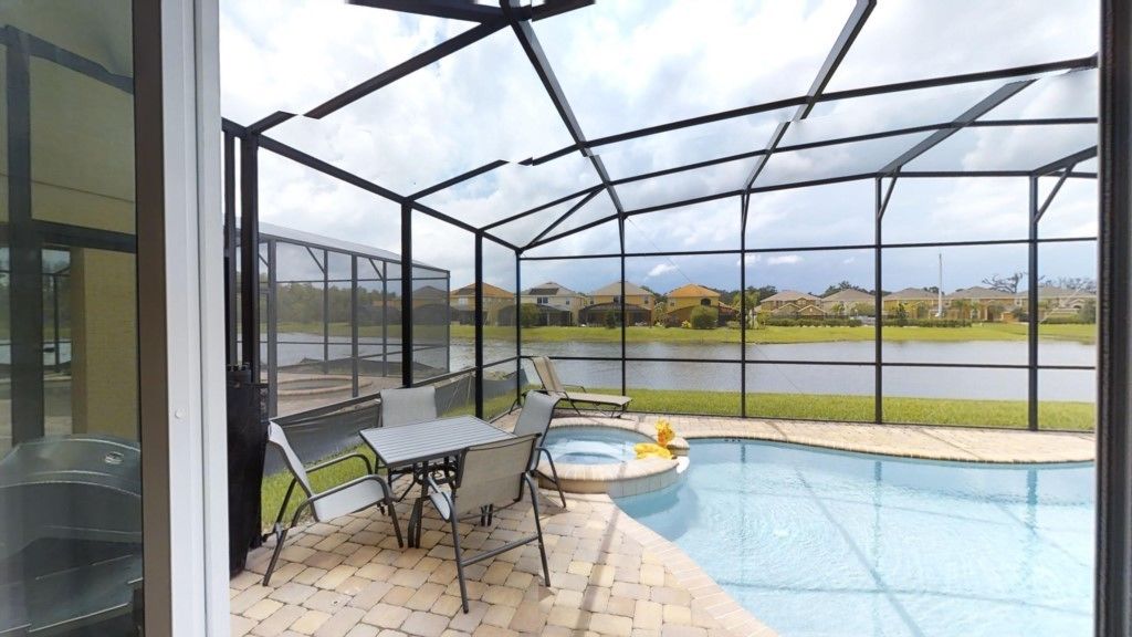 Un espace extérieur abrité comprenant une piscine, du mobilier de jardin et une vue sur un lac et des maisons au loin.