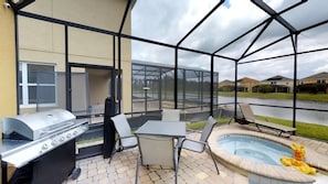 A covered patio area with a grill, seating, and a hot tub.