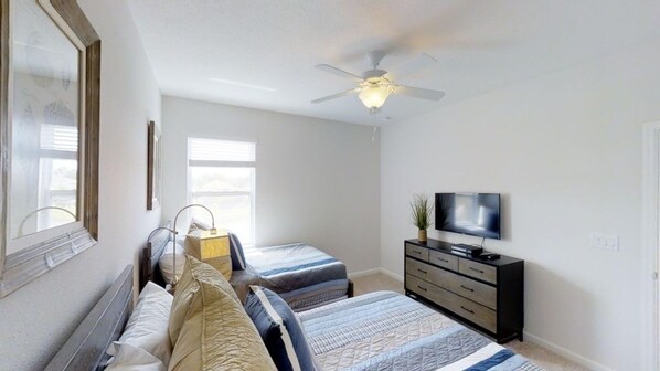 Une chambre avec deux lits, un ventilateur de plafond, une télévision et une commode.