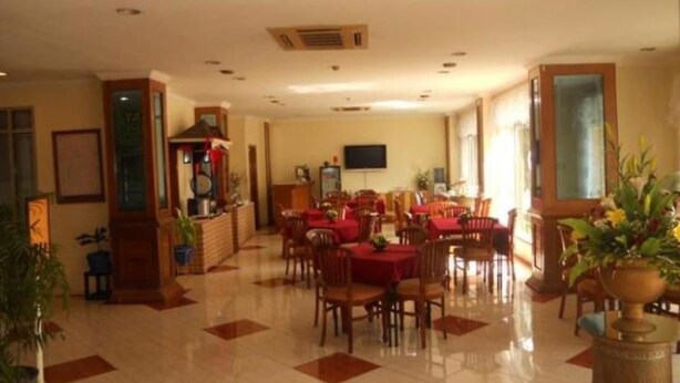 Un vestíbulo de hotel espacioso con suelo de baldosas, varias mesas de comedor con manteles rojos y un televisor montado en la pared.