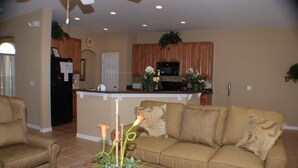 A living room with a beige sofa, a coffee table with a plant, and a kitchen area with wooden cabinets and a microwave. - Ip60215 - Sand Hill - 5 Bed 3 Baths Villa (Davenport)